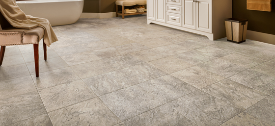 Gray luxury vinyl tile bathroom floor with cabinet and bathrub in the background